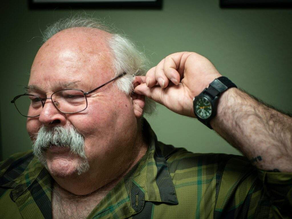 A man touching his ear as the 5 early signs of hearing loss are showing