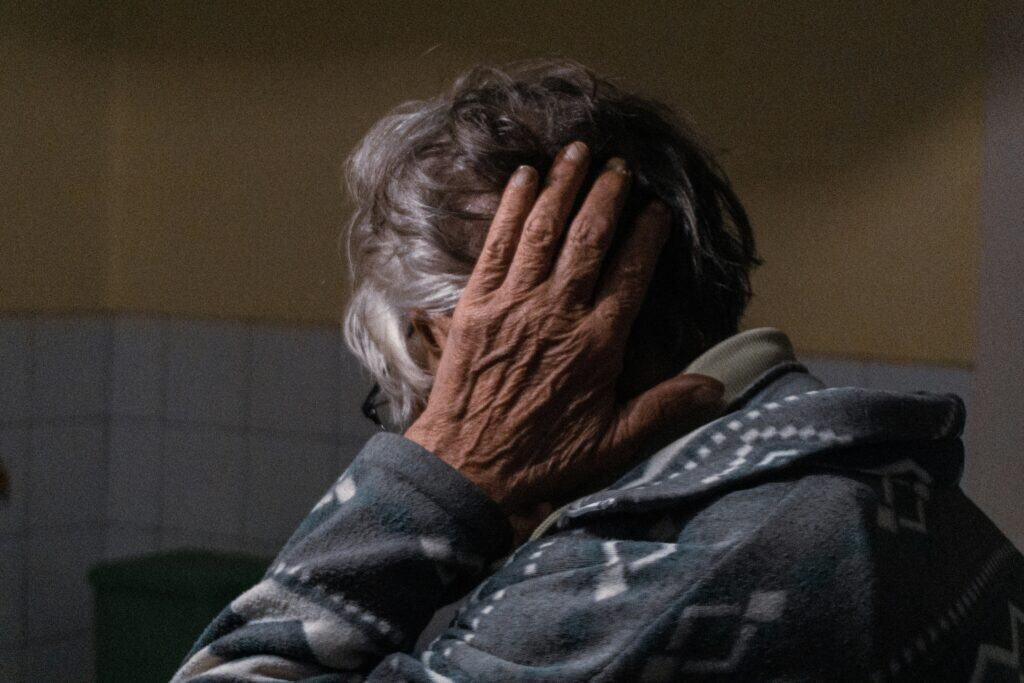 Close-up of a senior man with gray hair, hand covering face, feeling distressed or overwhelmed, showing signs of hearing loss in seniors.